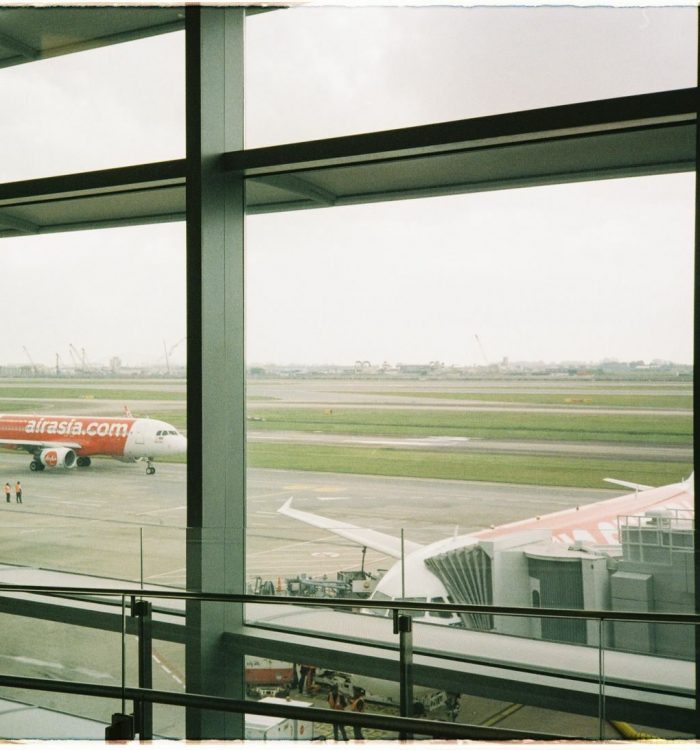 View of an AirAsia plane taxiing on the runway from inside the airport terminal.